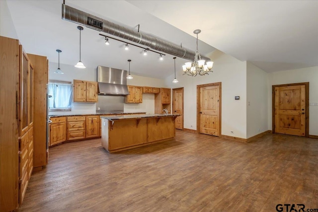 kitchen with hardwood / wood-style floors, wall chimney range hood, decorative light fixtures, and a kitchen island