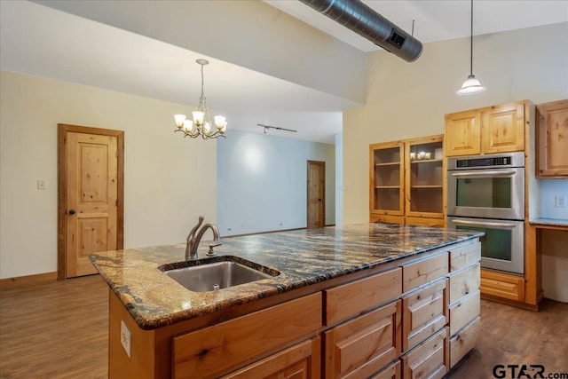 kitchen with dark wood-type flooring, a notable chandelier, sink, an island with sink, and stainless steel double oven