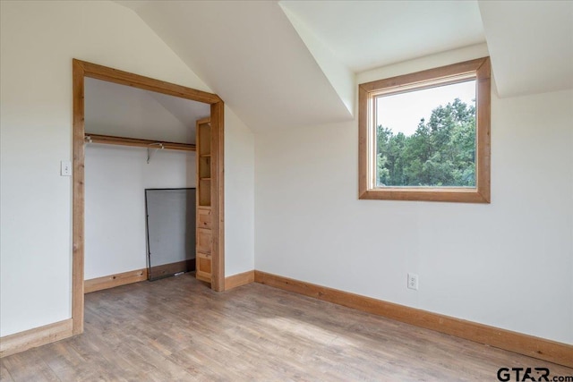 unfurnished bedroom featuring light hardwood / wood-style flooring, lofted ceiling, and a closet