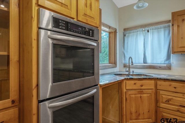 kitchen with sink, stainless steel double oven, and light stone countertops