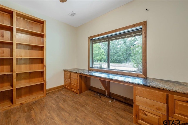 unfurnished office featuring hardwood / wood-style floors and built in desk