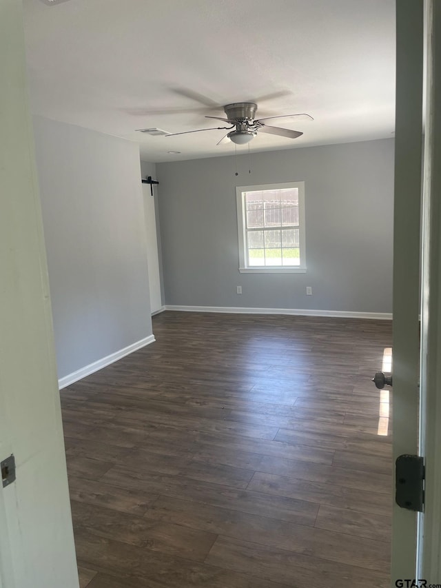 spare room featuring dark wood-type flooring, a barn door, and ceiling fan