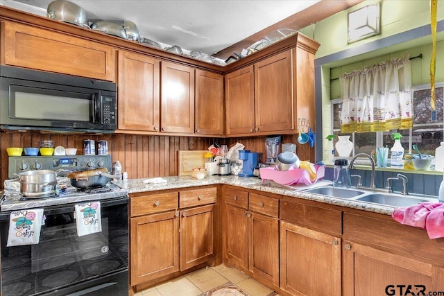 kitchen featuring light stone counters, light tile patterned floors, brown cabinetry, a sink, and black appliances