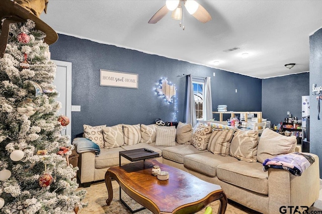 living room featuring ceiling fan, visible vents, and a textured wall