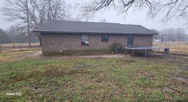 back of house featuring a trampoline, cooling unit, and a lawn