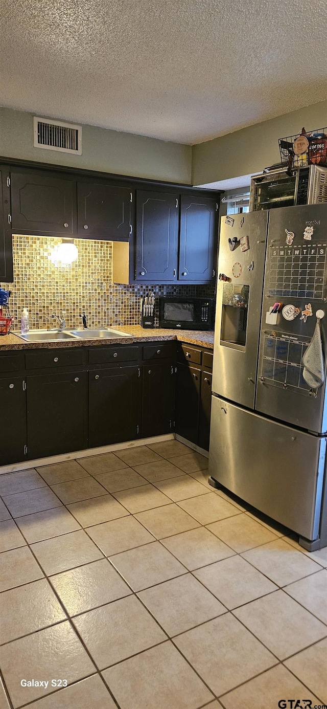 kitchen with stainless steel refrigerator with ice dispenser, light tile patterned flooring, a textured ceiling, and decorative backsplash