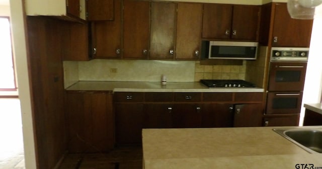915 John St, Jacksonville, TX 75766 - kitchen with stainless steel microwave, multiple ovens, black gas stovetop, backsplash, and light countertops