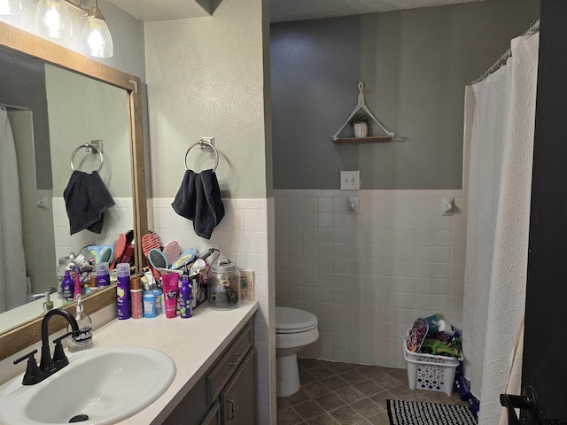 bathroom with toilet, tile walls, vanity, a wainscoted wall, and tile patterned flooring