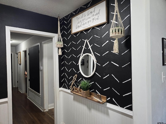 hall featuring a wainscoted wall, an accent wall, wood finished floors, and a textured ceiling