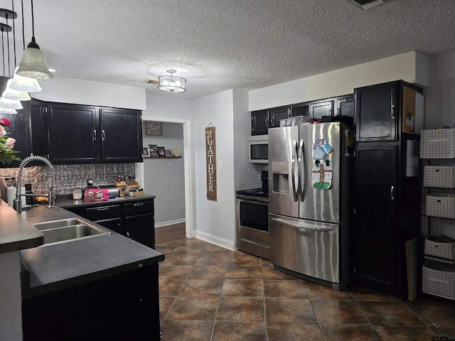 kitchen with dark countertops, dark cabinetry, decorative backsplash, stainless steel appliances, and a sink