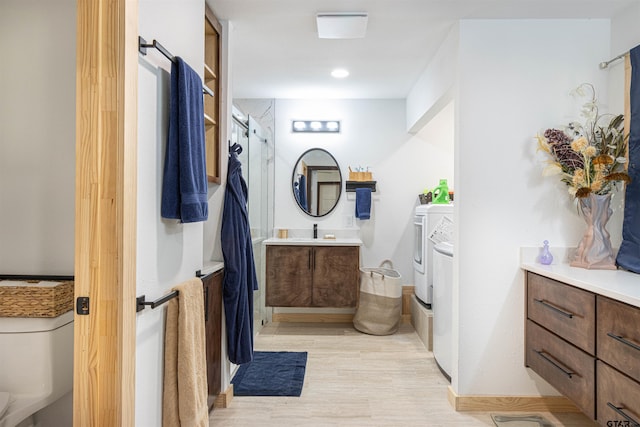 bathroom featuring toilet, vanity, wood finished floors, walk in shower, and independent washer and dryer