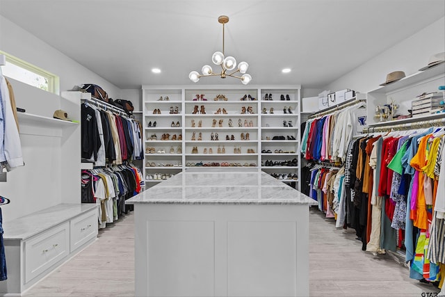 walk in closet with light hardwood / wood-style flooring and an inviting chandelier