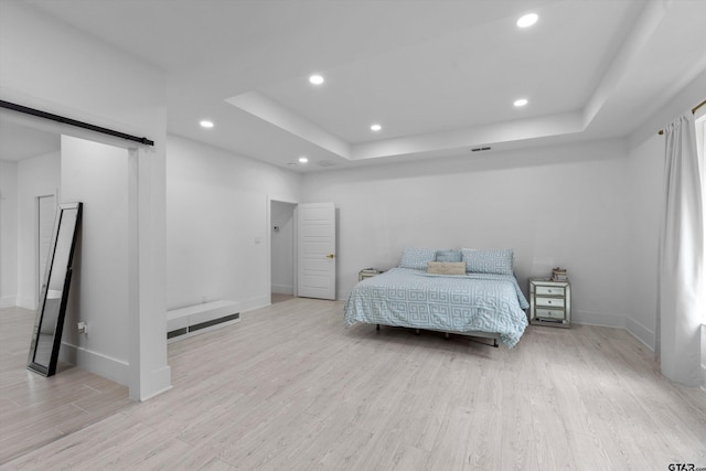 bedroom with a barn door, a raised ceiling, and light wood-type flooring