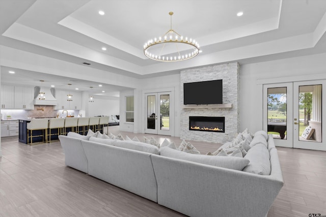 living room with french doors, a fireplace, a notable chandelier, and a tray ceiling