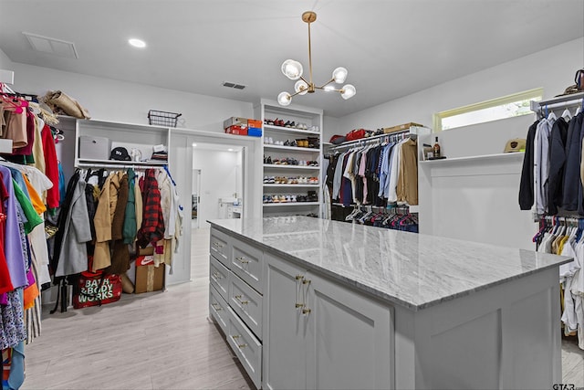 spacious closet with light hardwood / wood-style floors and a chandelier