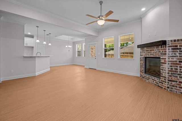 unfurnished living room featuring a brick fireplace, light hardwood / wood-style floors, ceiling fan with notable chandelier, and crown molding