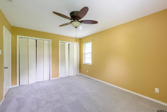 unfurnished bedroom with multiple closets, light colored carpet, and ceiling fan