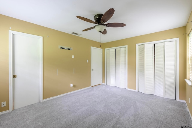 unfurnished bedroom featuring carpet flooring, two closets, and ceiling fan