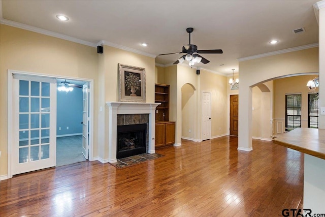 unfurnished living room with wood-type flooring, a tile fireplace, ceiling fan, and crown molding