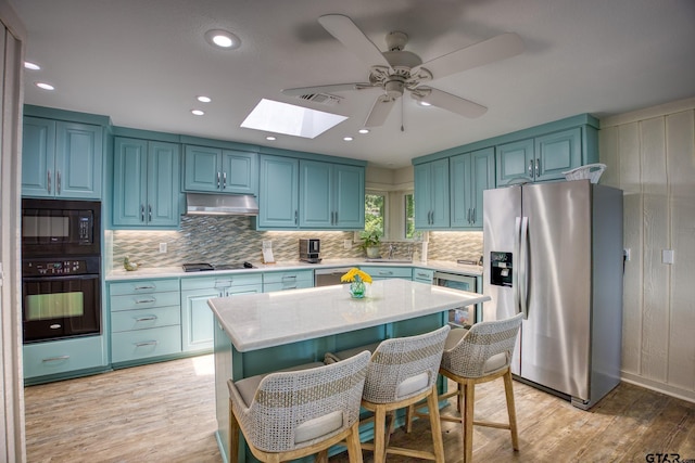 17553 Sleepy Hollow Way, Flint, TX 75762 - kitchen featuring black appliances, a skylight, under cabinet range hood, light wood-style floors, and blue cabinetry