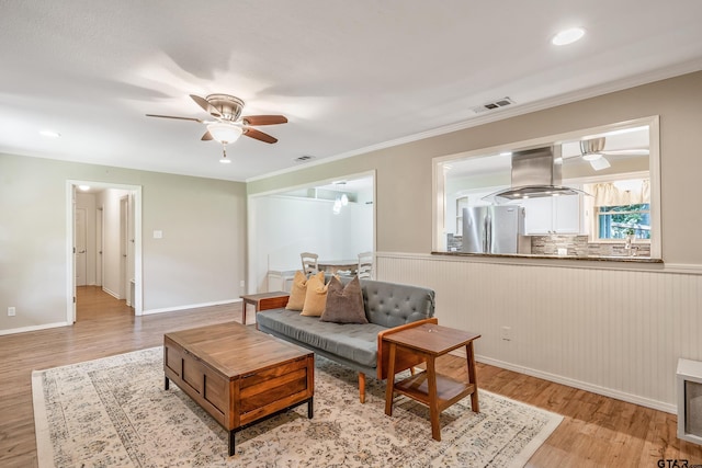 living room featuring a ceiling fan, light wood finished floors, wainscoting, ornamental molding, and recessed lighting