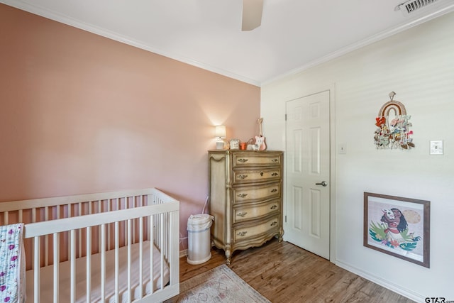 bedroom featuring wood finished floors, ornamental molding, ceiling fan, and a crib