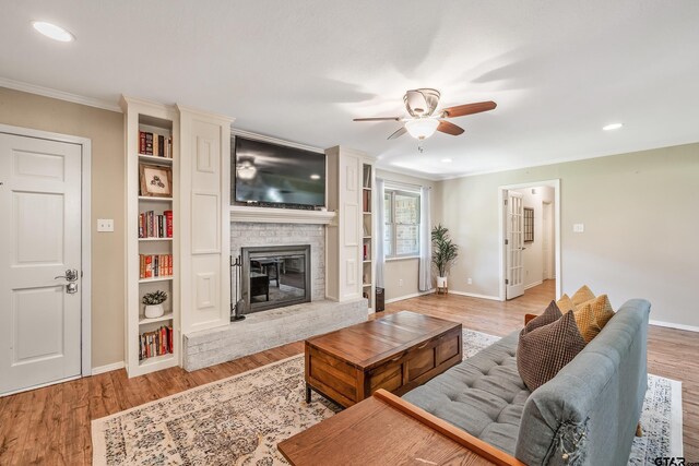 living room with ceiling fan, ornamental molding, a fireplace, baseboards, and light wood-type flooring