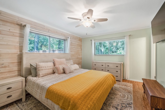 bedroom featuring light wood-style flooring, wood walls, ornamental molding, ceiling fan, and baseboards