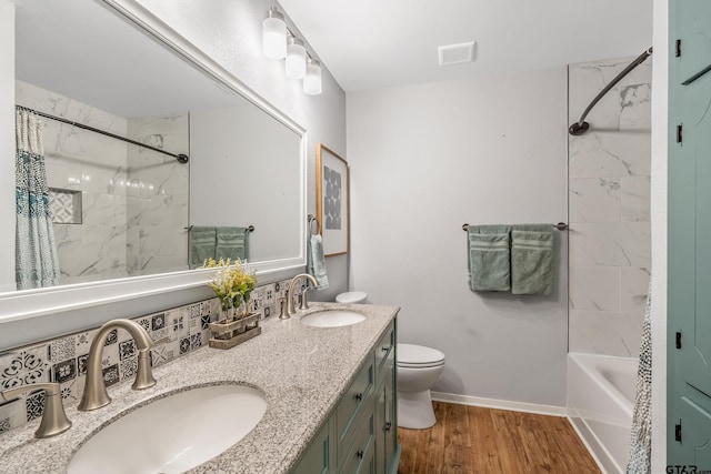 full bath with wood finished floors, baseboards, toilet, double vanity, and tasteful backsplash