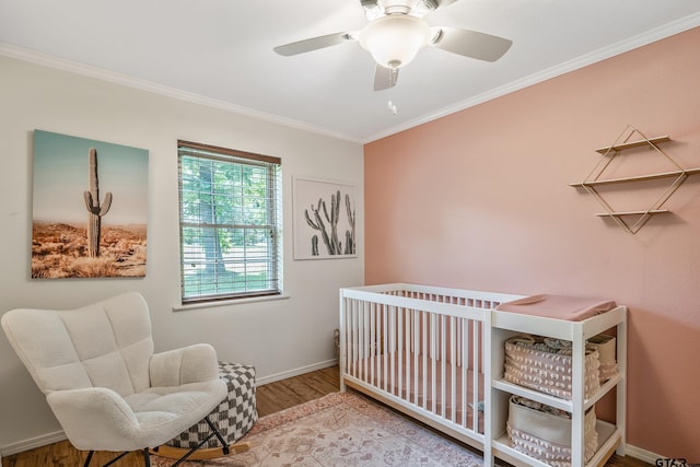 bedroom with crown molding, a nursery area, wood finished floors, baseboards, and ceiling fan