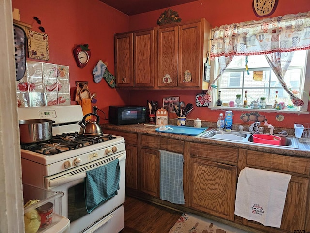 kitchen with white gas range oven, black microwave, brown cabinetry, a sink, and wood finished floors