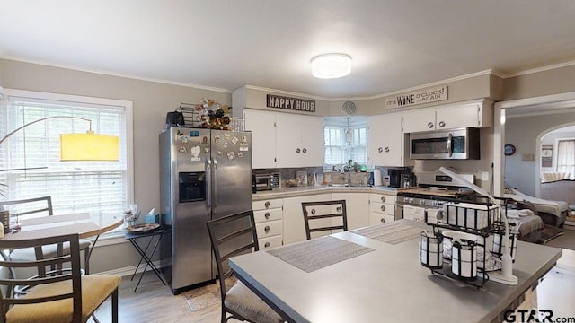 kitchen with stainless steel appliances, white cabinetry, ornamental molding, a sink, and light wood-style floors