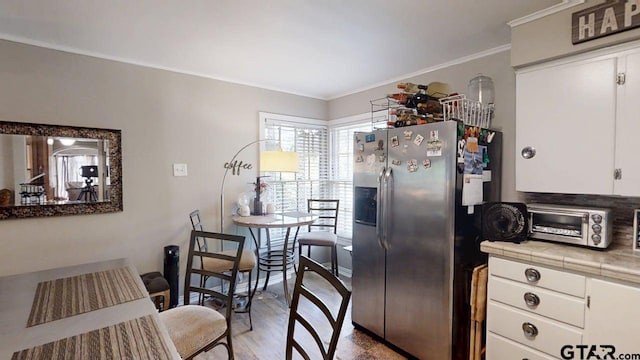 kitchen featuring stainless steel fridge, tile counters, white cabinets, and crown molding