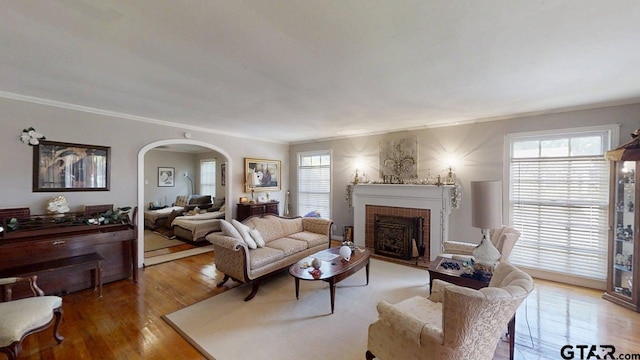 living room with arched walkways, crown molding, a fireplace, and wood finished floors