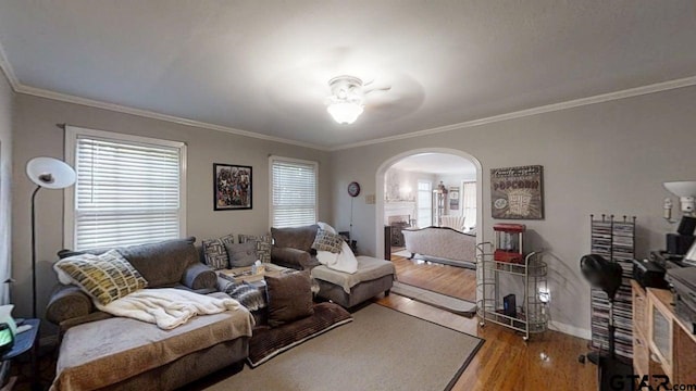 living area with arched walkways, ornamental molding, wood finished floors, baseboards, and a ceiling fan
