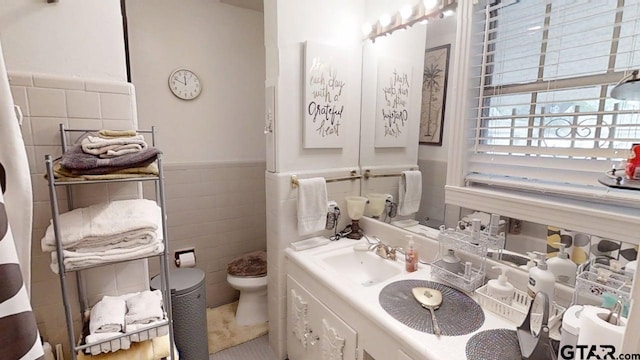 bathroom featuring toilet, tile walls, a wainscoted wall, and vanity