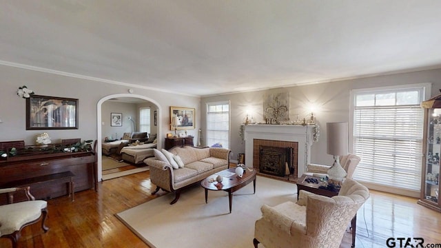 living area featuring arched walkways, a fireplace, ornamental molding, healthy amount of natural light, and wood finished floors