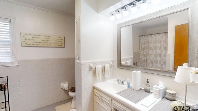 full bath featuring tile walls, toilet, vanity, ornamental molding, and wainscoting