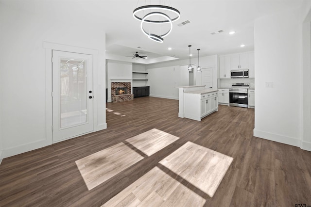 kitchen with appliances with stainless steel finishes, dark wood-type flooring, decorative light fixtures, white cabinets, and a center island