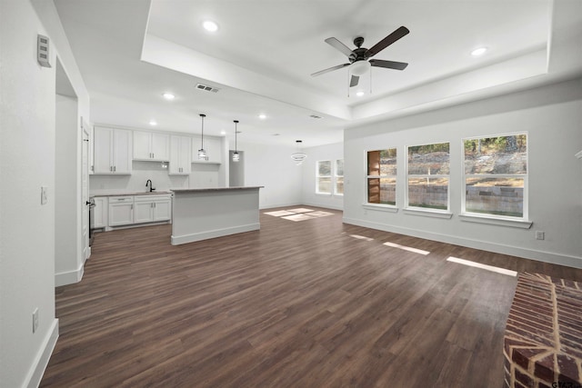 unfurnished living room with a raised ceiling, ceiling fan, dark wood-type flooring, and sink