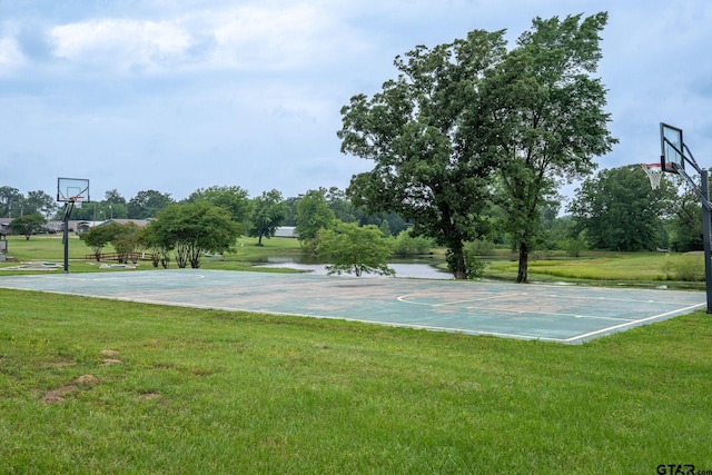 view of sport court with a water view and a yard