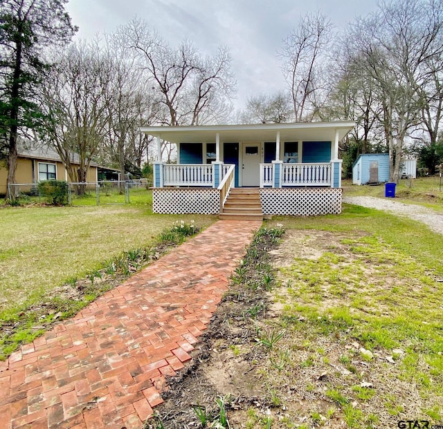 view of front of property featuring a front lawn, covered porch, and a shed