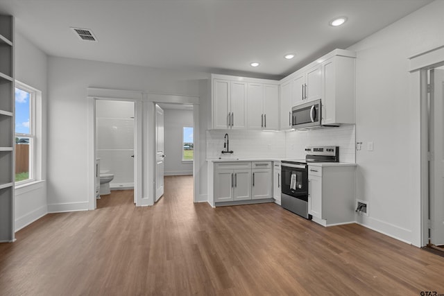 kitchen with light wood-type flooring, white cabinetry, a healthy amount of sunlight, and stainless steel appliances