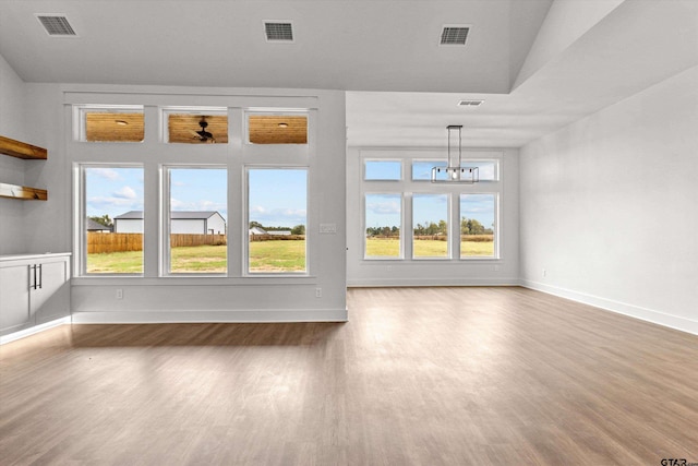 unfurnished living room featuring hardwood / wood-style flooring, a healthy amount of sunlight, and a notable chandelier