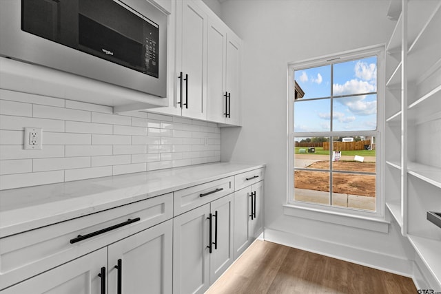 kitchen featuring black microwave, light stone countertops, white cabinetry, and decorative backsplash