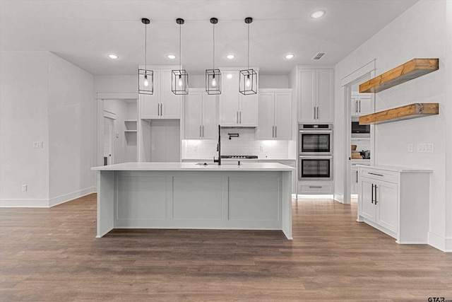 kitchen featuring a center island with sink, white cabinets, hardwood / wood-style floors, hanging light fixtures, and double oven