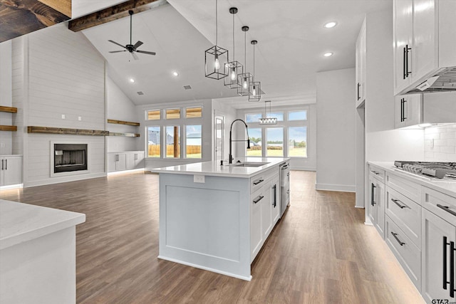 kitchen with a center island with sink, high vaulted ceiling, white cabinetry, appliances with stainless steel finishes, and decorative light fixtures