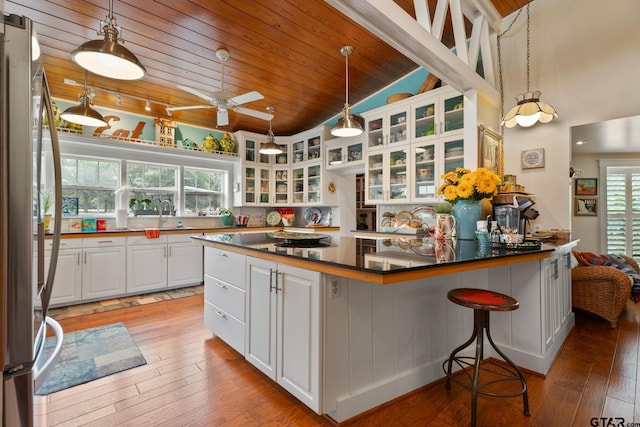 kitchen featuring a kitchen bar, white cabinets, wooden ceiling, ceiling fan, and light wood-type flooring