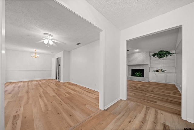 608 Meadow Crk, Tyler, TX 75703 - unfurnished living room with a chandelier, a textured ceiling, light wood finished floors, a ceiling fan, and a brick fireplace