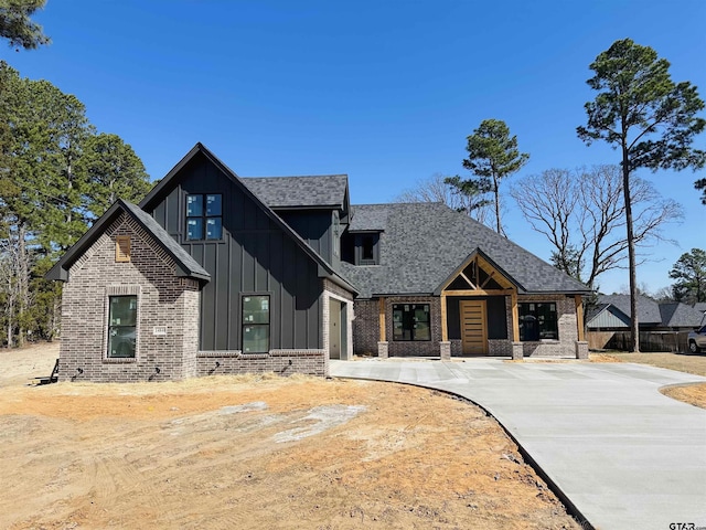 modern farmhouse with roof with shingles, brick siding, board and batten siding, and driveway